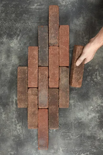 Hand places Belgian brick at top of lop-sided lozenge comprising 11 Antique Red Brick Pavers, part of our Alpha Clay Paving range.