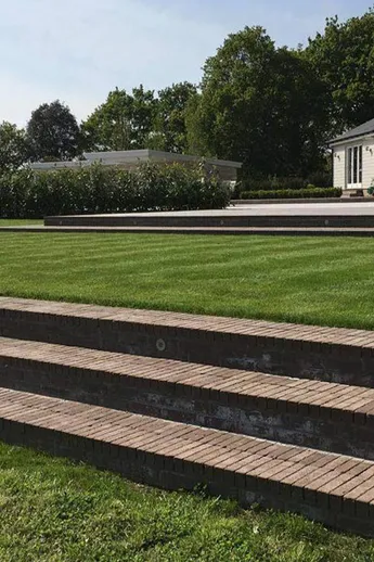 3 long steps of Aldridge Brick pavers set into large lawn. House with patio and sunloungers behind. Built by C + S Construction.
