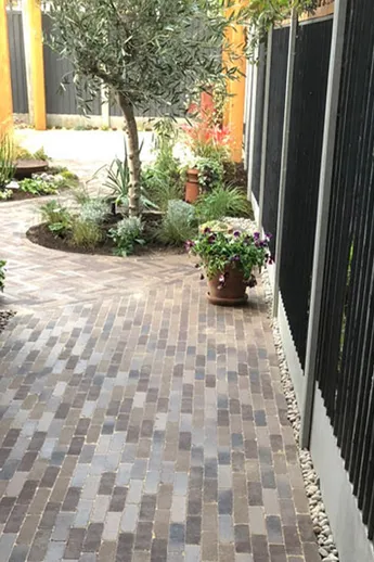 Aldridge Brick Pavers laid between side of house and fence, leading to paved garden with round bed. Design by Harrison Gardens.