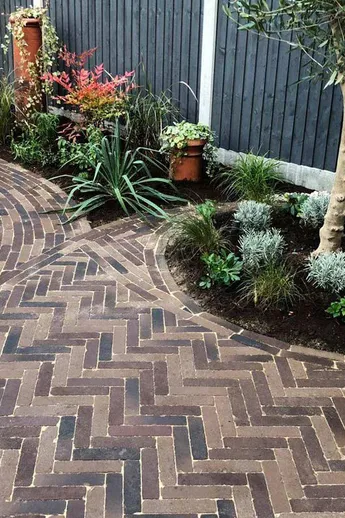 Aldridge Clay Pavers laid herringbone and running bond between curved beds with olive tree, water feature and chimney pot planters.