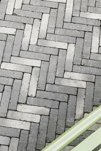 Silver Grey Multi Belgian Bricks, laid herringbone, partly seen through slats of green wooden bench. Design by Cadogan Landscapes.
