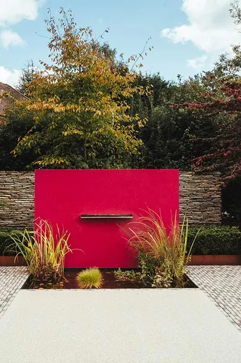 Silver Grey Multi clay pavers edge water feature with red wall and planted pond. Design by Nic Howard. Built Langdale Landscapes.