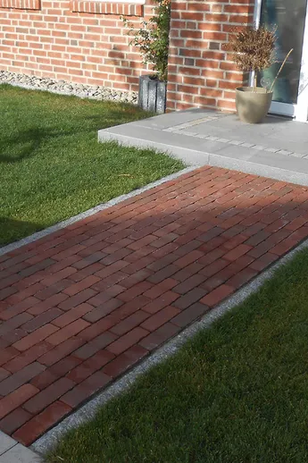 Short path Novara Dutch Clay Pavers edged with gravel leads across lawn from pavement to porch step of house with open door.
