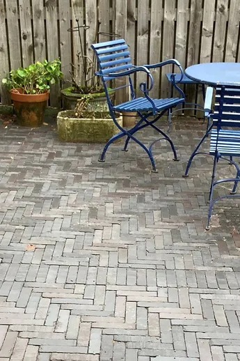Blue wooden slatted bistro chairs with table sit on Moderna Dutch Clay Pavers next to tall fence. Built by Gray Stone Works.