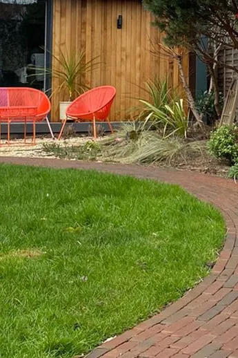 Path of Winton Brick Pavers curves around lawn, leading to orange furniture in front of outdoor room. Design by Landscape Artisan.