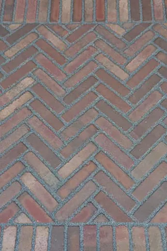 Red and brown Bexhill Brick Pavers with grey mortar joints, laid in herringbone pattern with soldier course borders by Plant Trap.