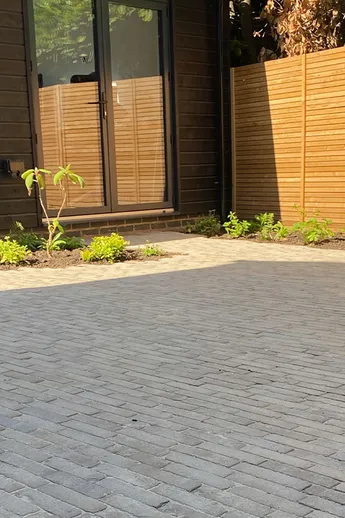 Back of modern house and shaded, fenced garden paved in Charcoal Grey Clay Pavers by Scholey Garden Design and Pots of Style
