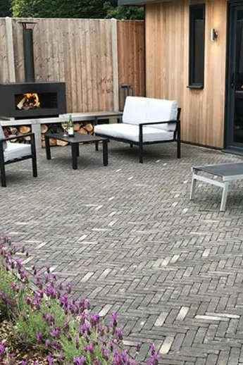 Outdoor lounge set, woodburner and 2 sunloungers on patio of Silver Grey Multi Clay Pavers, with border of lavender and box.
