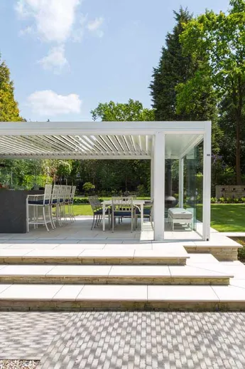Impressive view of white pergola with bar and dining area, Silver Grey Multi Clay Pavers used as paving before set of light steps.